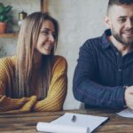 Couple securing a deal with handshake, smiling in a casual setting.