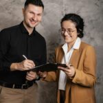 Two professionals finalize a real estate contract with a clipboard and pen.